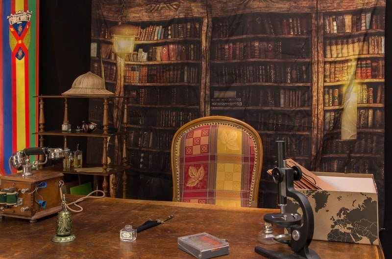 le bureau d'un explorateur est mis en scène avec un grand fauteuil coloré près d'un bureau, sur celui-ci un téléphone, un téléscope et un chapeau d'explorateur
